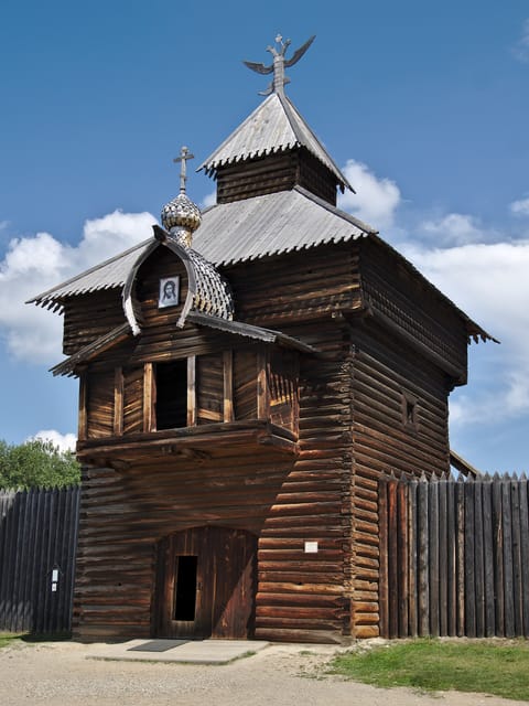 Деревянная проезжая башня с шатровой крышей, рядом частокол из брёвен