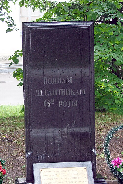 Тёмная гранитная стела с надписью «Воинам-десантникам 6-й роты», у подножия — табличка и цветы