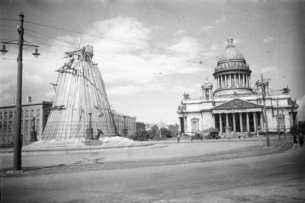 Исаакиевская площадь блокадного Ленинграда в 1942 году: пустая мостовая, памятник Николаю I укрыт высоким защитным коробом, за ним — Исаакиевский собор