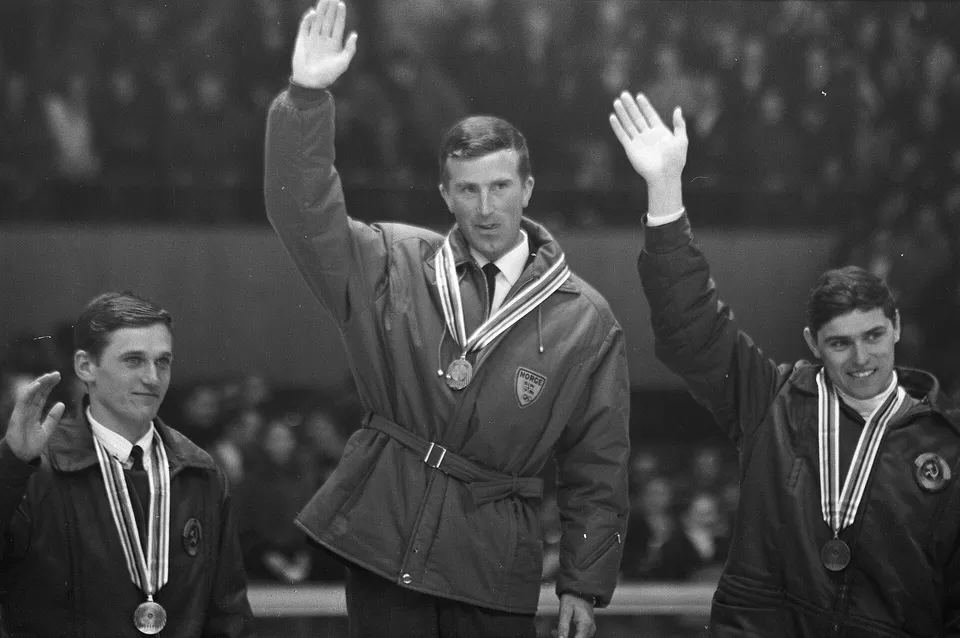 Чёрно-белое фото 1968 года: три биатлониста с медалями на шее машут руками с пьедестала в Гренобле